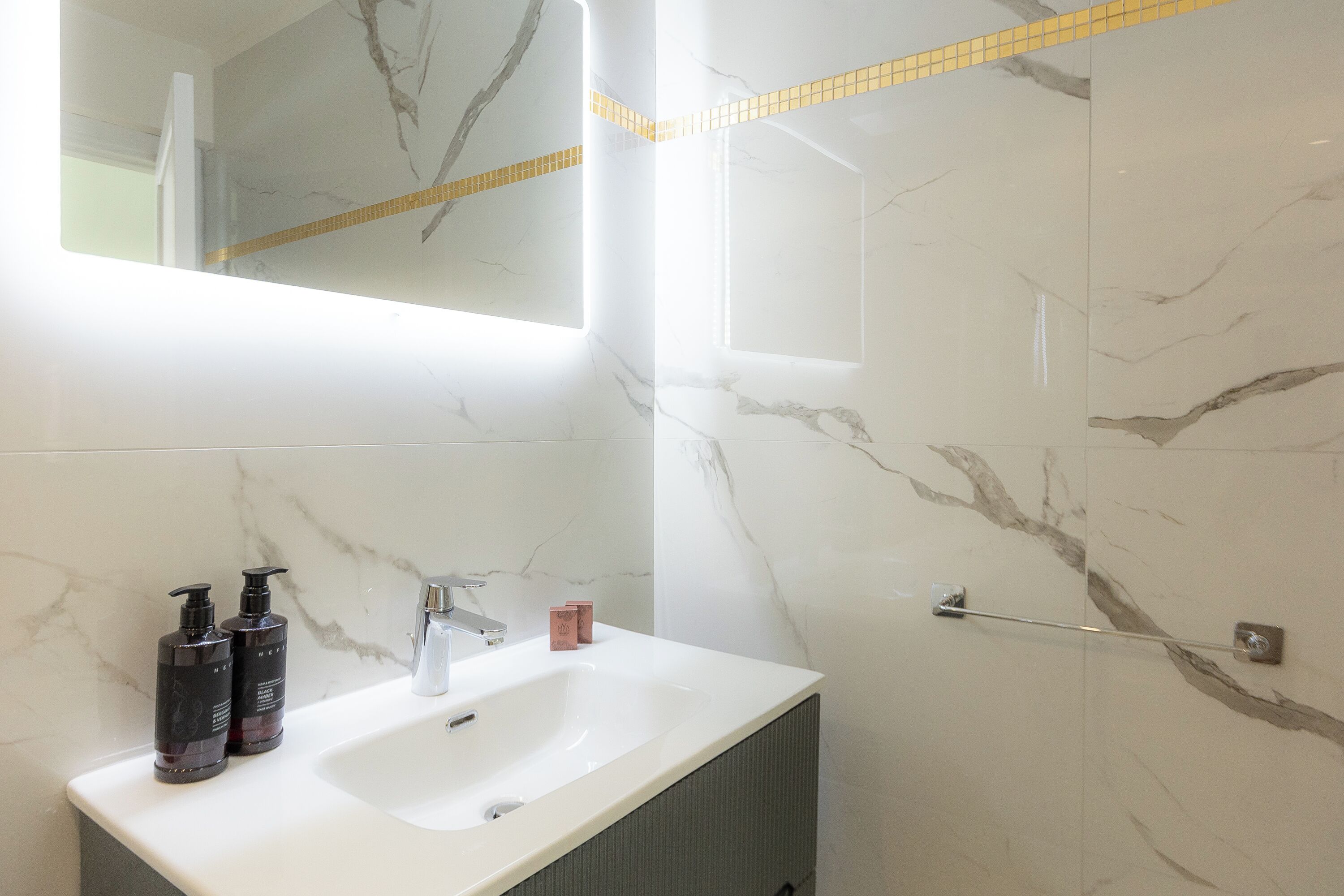 A bathroom with a white sink, two black soap dispensers, a mirror, and a towel rack.