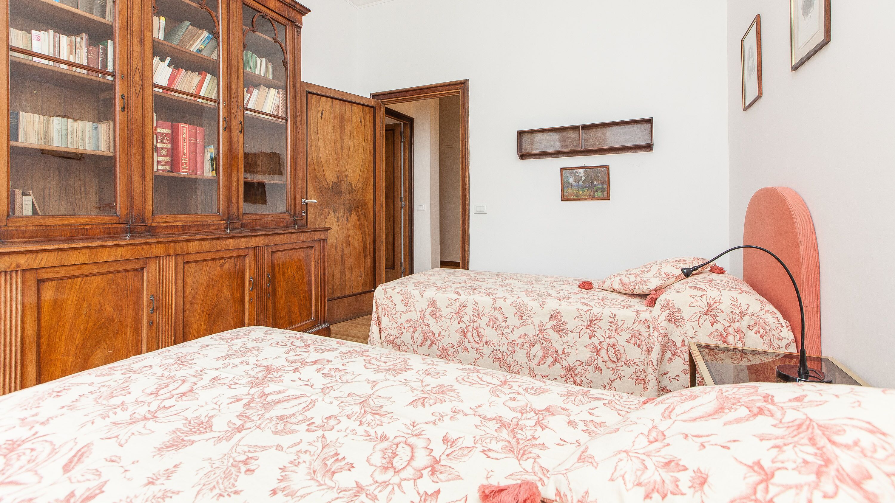 A bedroom with two beds, a wooden wardrobe, and a small bedside table.