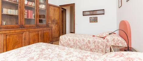 A bedroom with two beds, a wooden wardrobe, and a small bedside table.