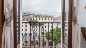 A view from a balcony with a wrought iron railing, overlooking a street with buildings and a tree.