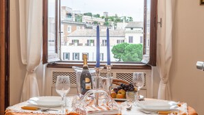 A dining table set with plates, glasses, a bottle, and candles, with a window view of buildings.