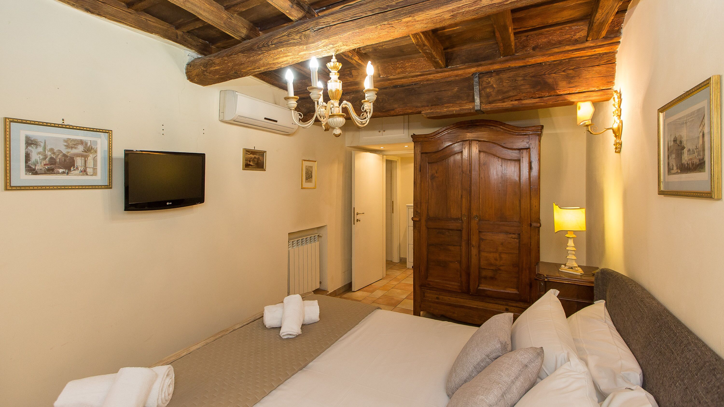 A hotel room with a wooden ceiling, a bed with pillows, a television, a door, and a wall-mounted air conditioner.