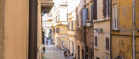 A narrow cobblestone street flanked by historic buildings with shuttered windows and a mix of architectural styles.