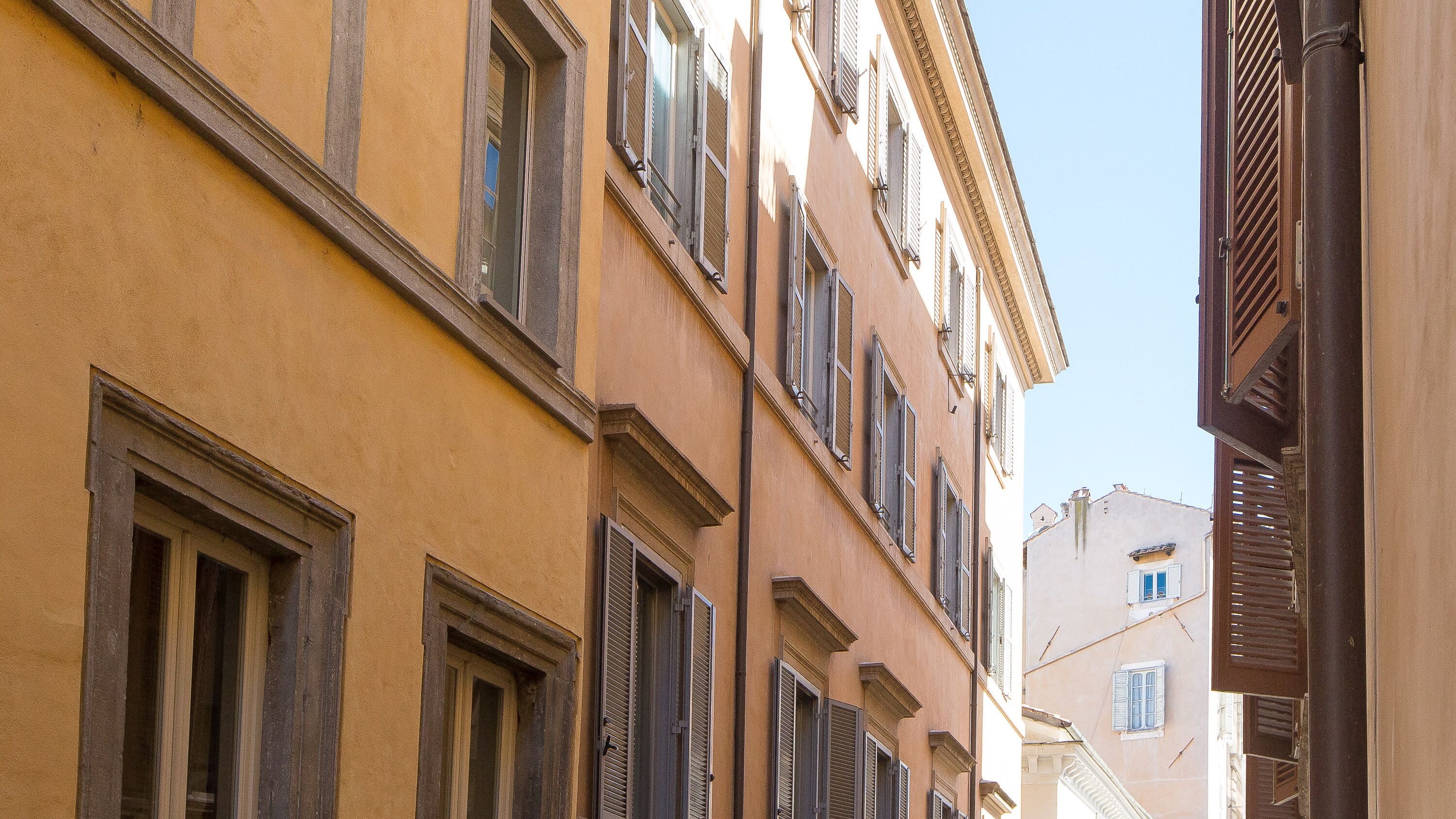 A narrow street with buildings featuring traditional architecture, including shuttered windows and balconies.