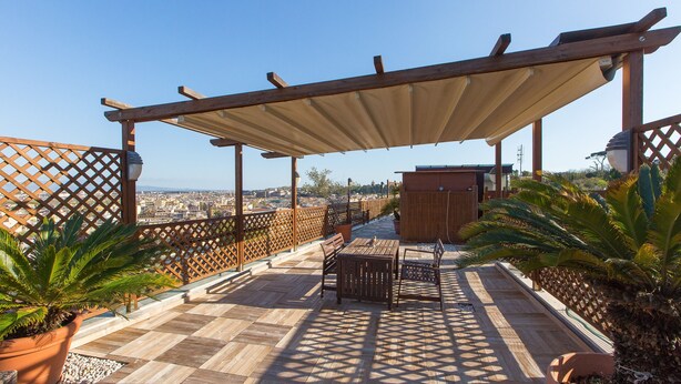 Una terrazza sul tetto con pergolato, zona salotto e piante in vaso.