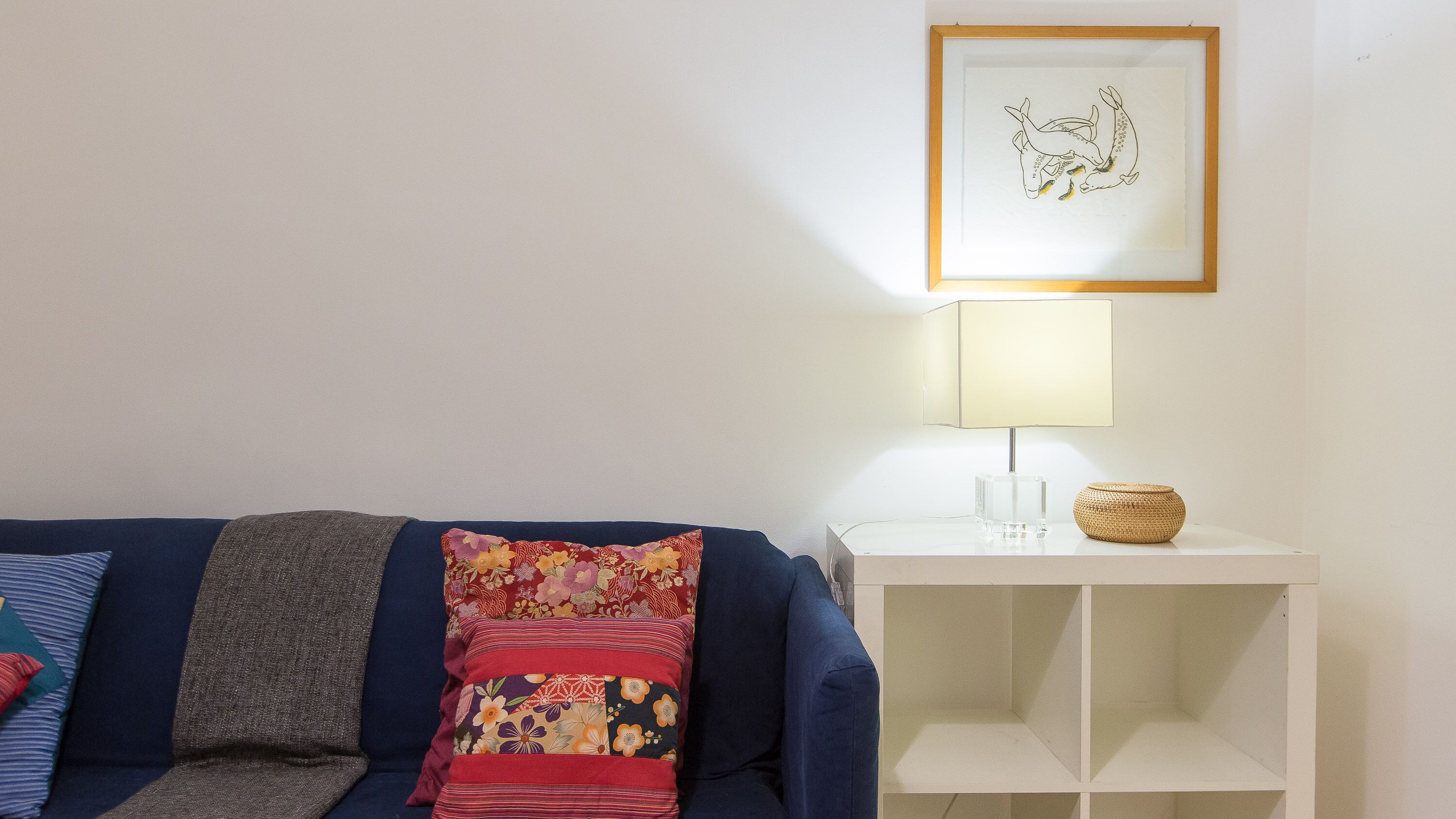 A living room with a blue sofa, a white side table, a framed picture, and a lamp.