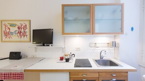A compact kitchen with a sink, a coffee maker, and a flat-screen TV on a shelf.