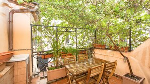 A small outdoor patio with a wooden table and chairs, surrounded by potted plants and a metal fence. - Rental in Rome Scala Deluxe Terrace (Rome)
