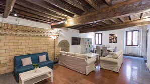 A living room with a brick wall, a blue sofa, a white sofa, and a dining area with a table and chairs. - Rental in Rome Scala Deluxe Terrace (Rome)