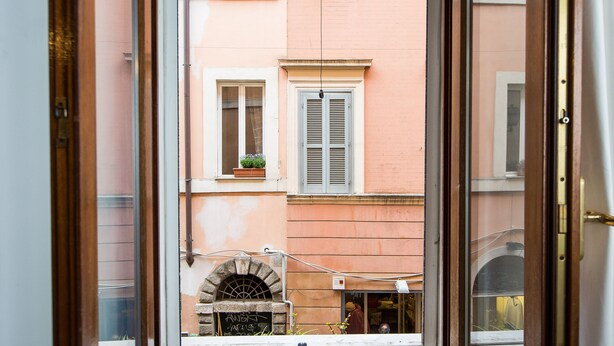 A view through an open door of a building with a stone archway, a window with shutters, and a small balcony with a potted plant. - Rental in Rome Scala Deluxe Terrace (Rome)