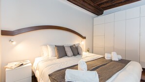 A neatly made bed with pillows and a blanket, a bedside table with a lamp, and a wardrobe with sliding doors. - Rental in Rome Scala Deluxe Terrace (Rome)