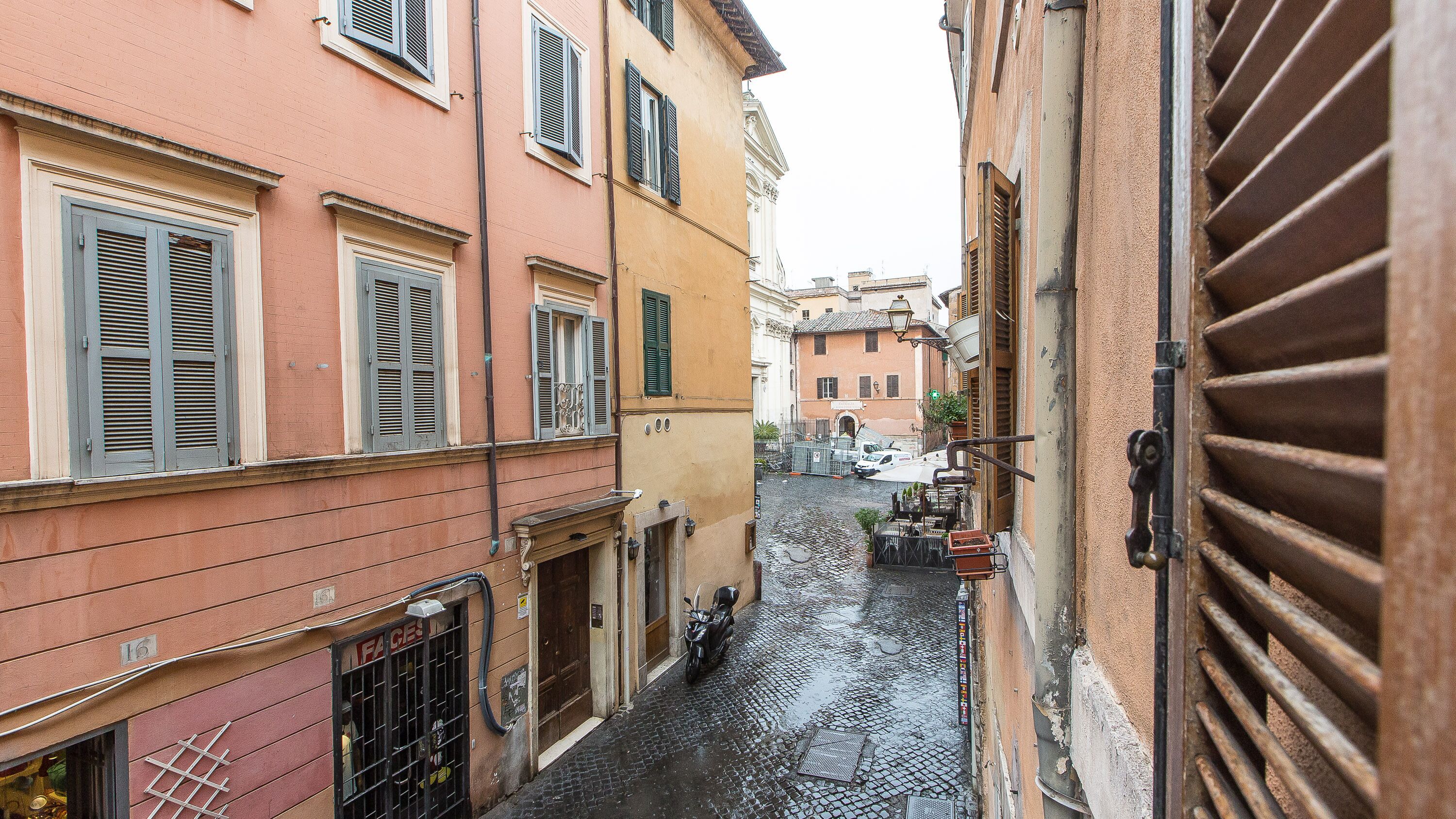 A narrow street with buildings on either side, a motorcycle parked on the right, and a cobblestone road.
