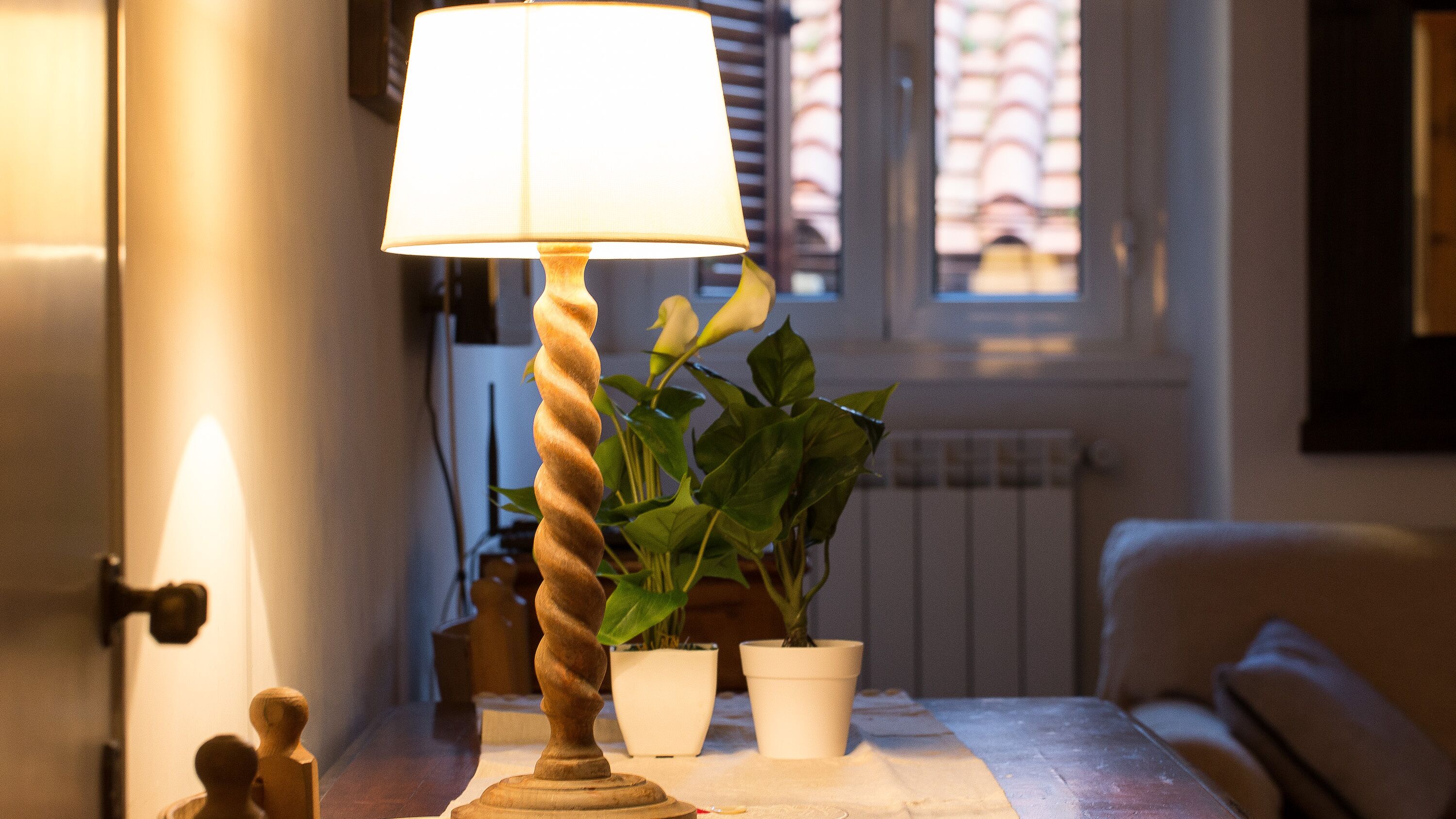 En lampe med snoet fod, et bord med hvid dug og to krukkeplanter.