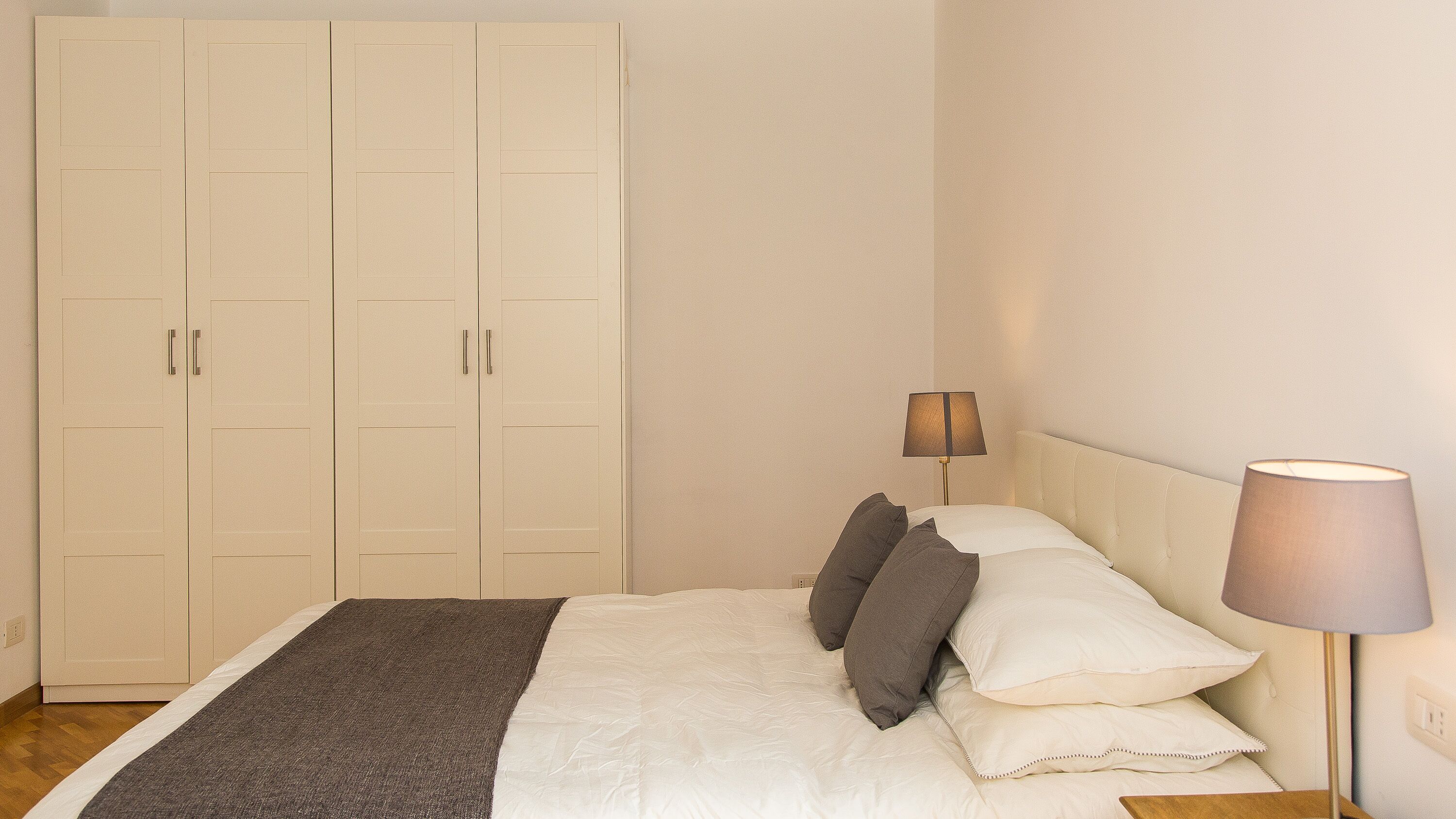 A bedroom with a bed, pillows, a bedside lamp, and a wardrobe.