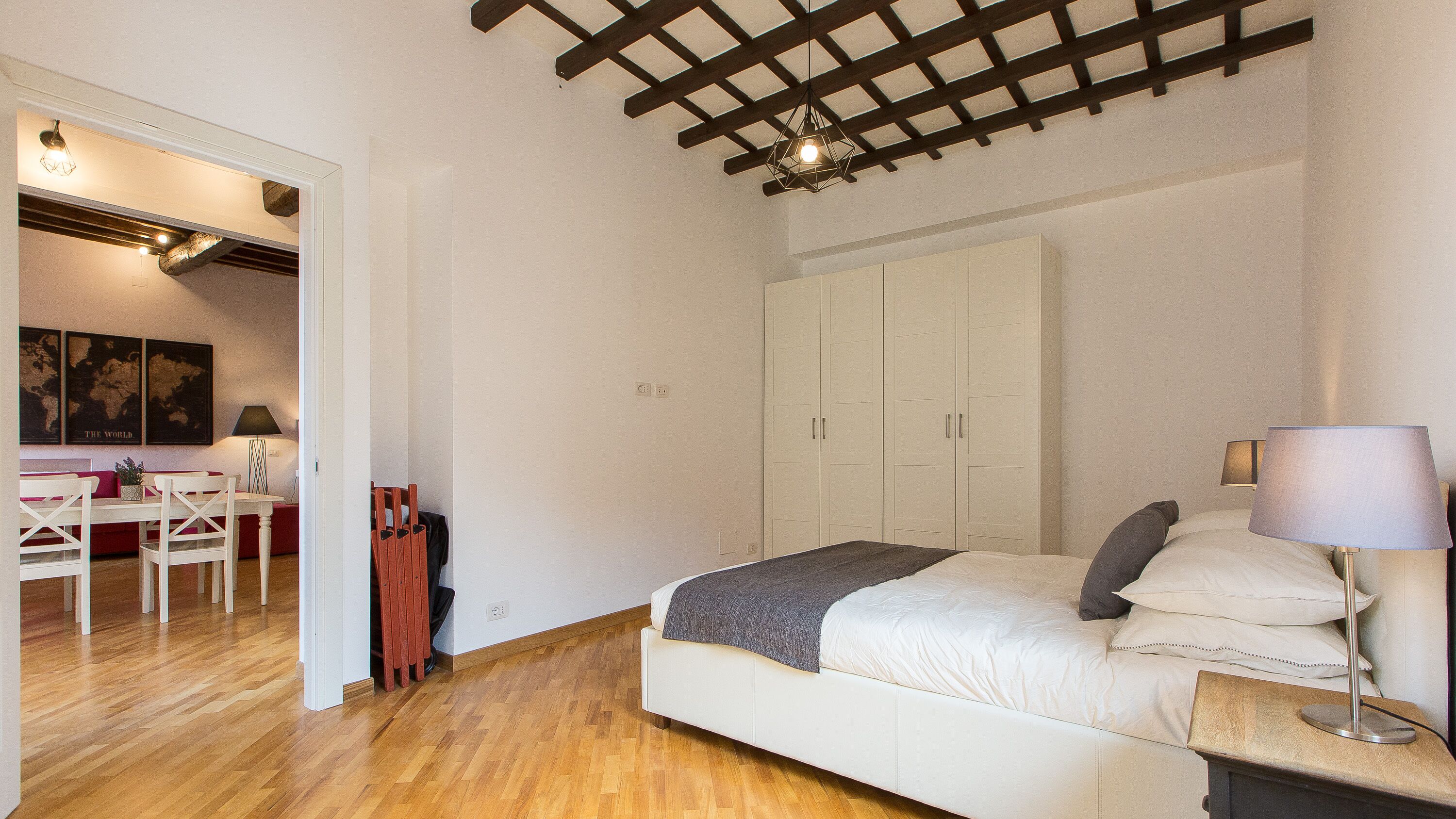 Een slaapkamer met een bed, nachtkastje, lamp, kledingkast en een zithoek met een tafel en stoelen.