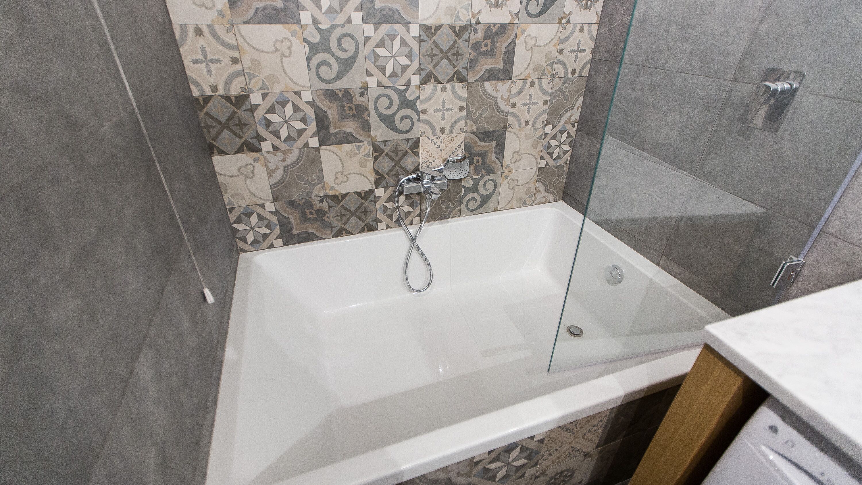 Un baño moderno con ducha envuelta en vidrio, una bañera blanca y azulejos estampados en las paredes.