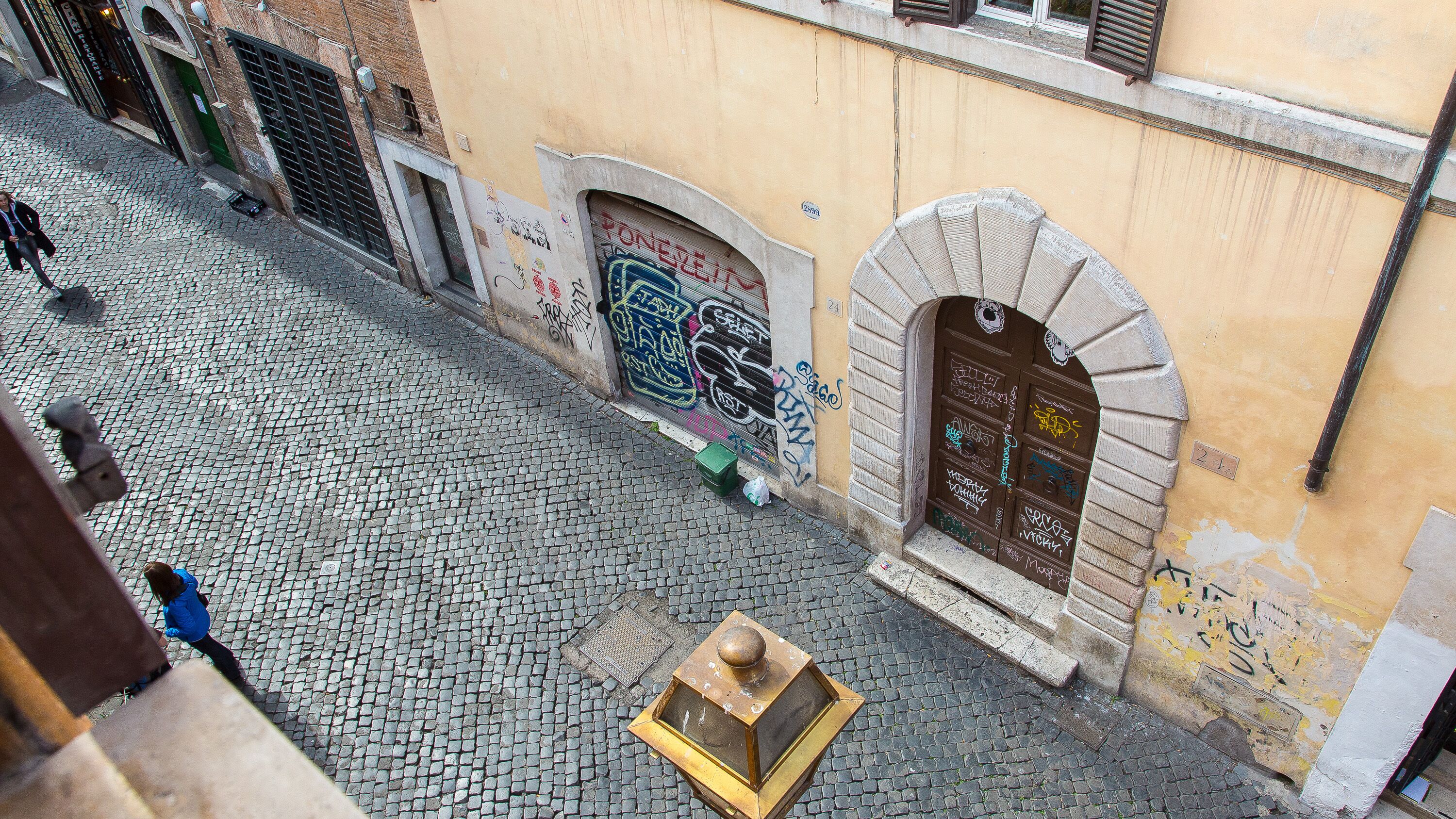 A cobblestone street with a building featuring a large arched doorway and a small square window.