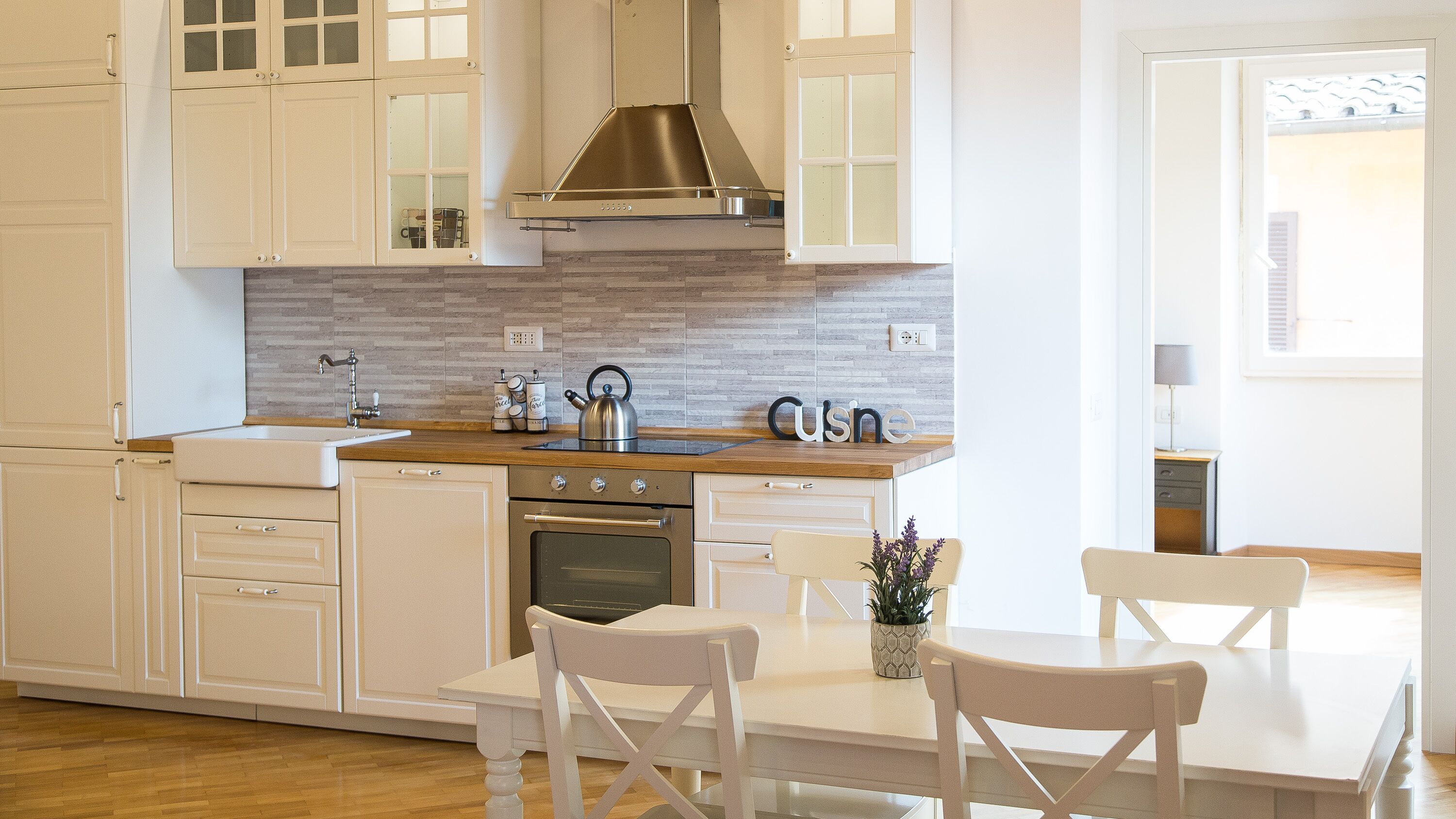 A modern kitchen with white cabinetry, a stainless steel range hood, and a wooden countertop.