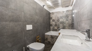 Une salle de bain moderne avec des carreaux gris, des toilettes blanches, un lavabo et un espace douche.