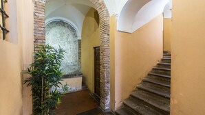 A narrow hallway with a brick wall, a wooden door, and a staircase leading upwards. - Rental in Rome Trastevere Atmosphere (Rome)