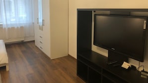 A hotel room with a bed, a TV on a stand, a wardrobe, and a window with curtains. - Apartmán Karla Čapka (Teplice)