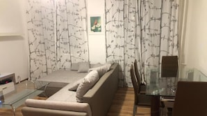 A modern living room with a sofa, a glass coffee table, and a dining area with a glass table and chairs. - Apartmán Karla Čapka (Teplice)