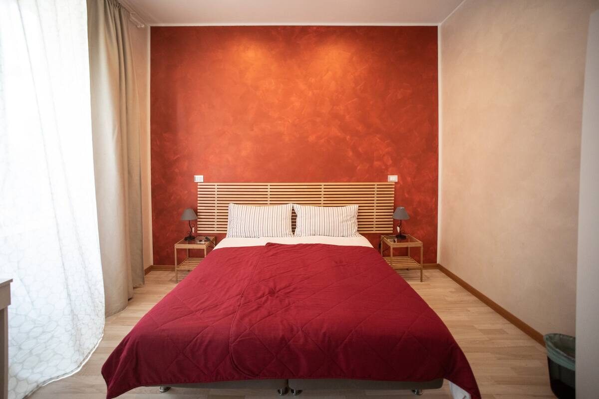 Une chambre avec un grand lit, une tête de lit en bois, deux tables de chevet avec des lampes et un mur rouge.