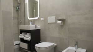 A modern bathroom with a toilet, bidet, sink, and a mirror. - Area39 (Trieste)