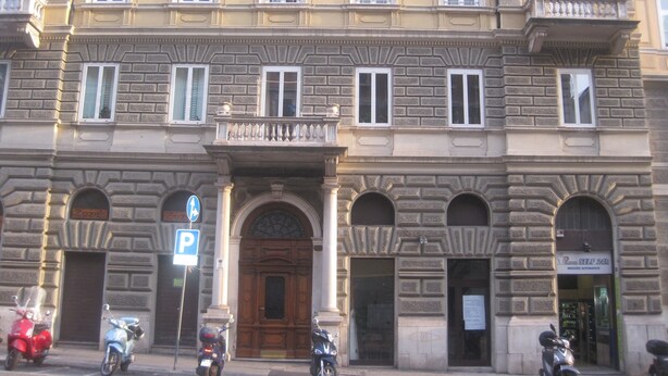 A historic building with a central entrance, multiple windows, and a parking sign. - Area39 (Trieste)