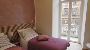 A bedroom with two beds, a wooden headboard, and a view of the street through a glass door. - Area39 (Trieste)