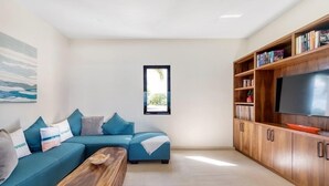 A modern living room with a sectional sofa, a coffee table, a TV, and a bookshelf. - Villa Amandara (Les Terres Basses)