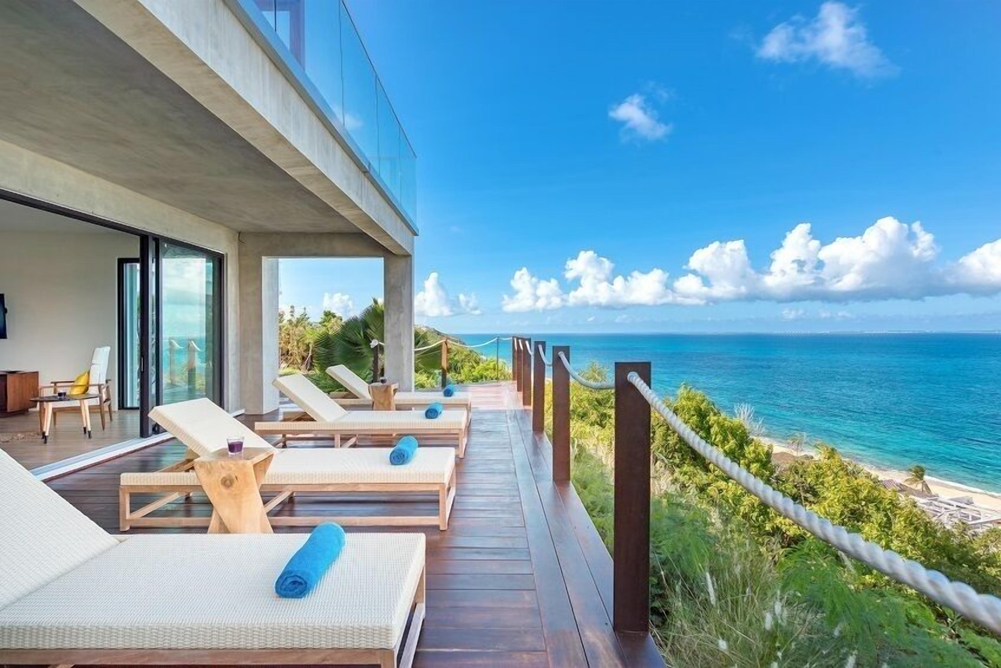 A deck with sun loungers overlooking a beach.