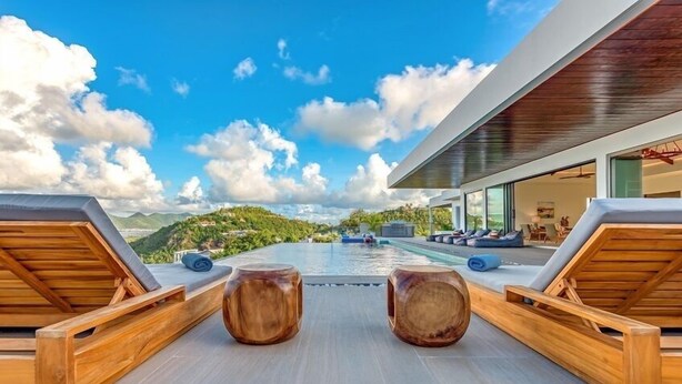 A modern outdoor pool area with wooden loungers and a view of a mountainous landscape. - Villa Amandara (Les Terres Basses)