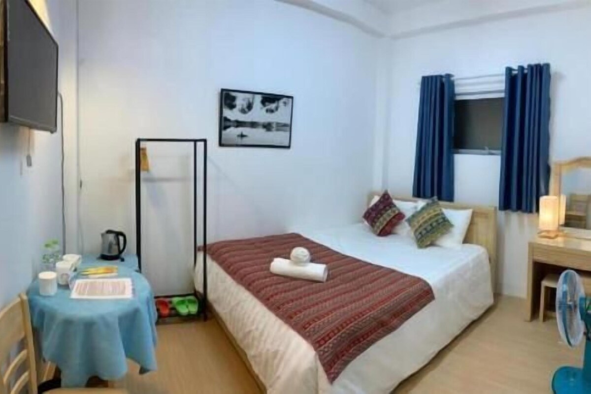 A hotel room with a bed, a desk, a chair, a TV, and a window with curtains.