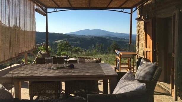Un patio exterior con una mesa y sillas, un sofá de mimbre y vistas a montañas distantes.