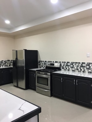 A kitchen with black cabinets, a stainless steel refrigerator, a gas stove, and a microwave. - Island Vibes Suites (Port of Spain)