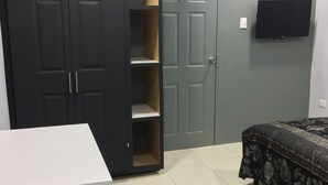 A bedroom with a bed, a wardrobe, a TV, and a desk. - Island Vibes Suites (Port of Spain)