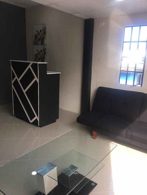 A reception area with a black and white geometric desk, a black sofa, and a glass table with a blue object.