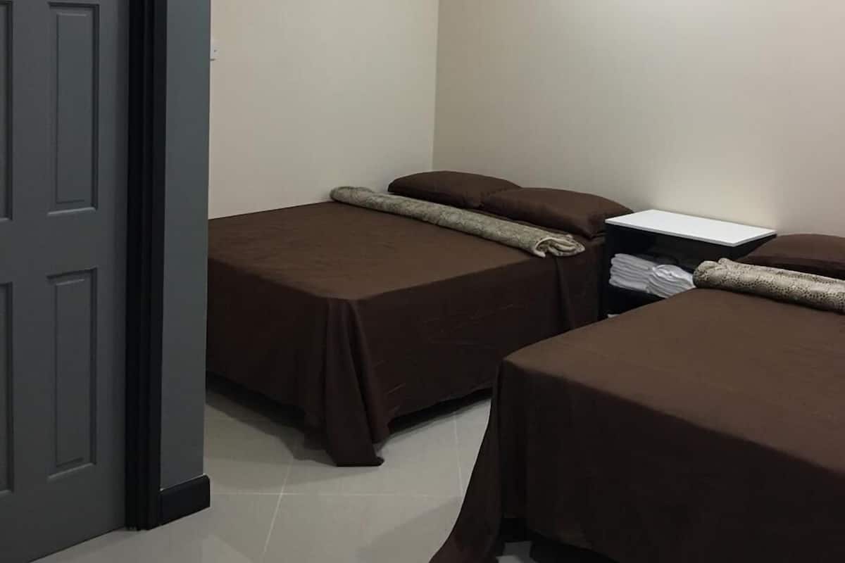 A room with two beds, a door, and a small table with a lamp.