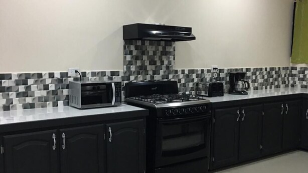 A kitchen with black cabinets, a gas stove, a microwave, and a coffee maker. - Island Vibes Suites (Port of Spain)