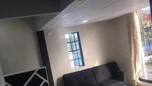 A modern living room with a black sofa, a glass coffee table, and a window with curtains. - Island Vibes Suites (Port of Spain)