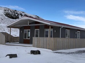 Un edificio moderno con entrada cubierta, cerca de madera y un paisaje nevado.