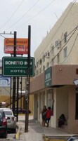 Un hotel llamado 'Bonito Inn' con un letrero que indica que es un hotel. Se ven personas afuera del edificio y un coche estacionado cerca.