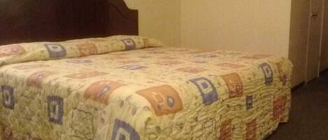 Una cama con colcha de diseños geométricos, cabecera de madera y un cuadro en la pared.