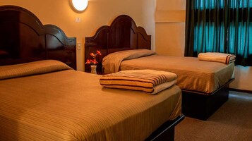 Dos camas individuales con cabeceros de madera, una mesita de noche con un florero y una ventana con cortinas.