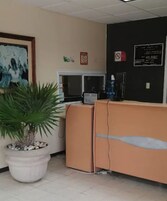 Zona de recepción con una planta en maceta, una computadora y una pizarra con texto.