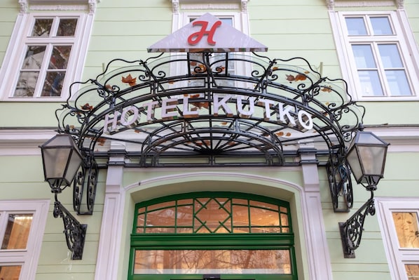 Entrada de un hotel con un letrero de hierro forjado que dice "HOTEL KUTKO".