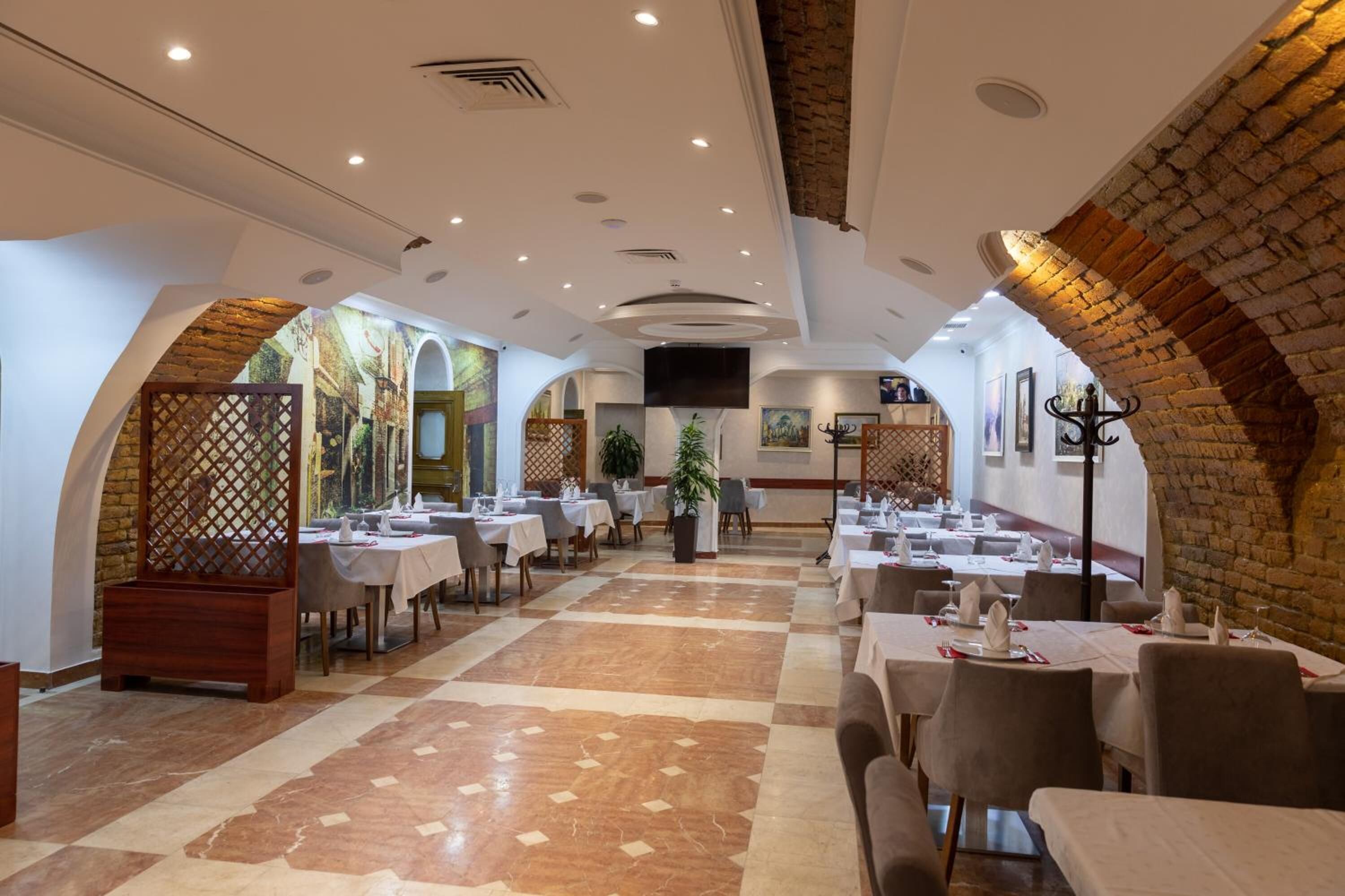 A spacious restaurant with high ceilings, exposed brick arches, and a checkered floor. Tables are neatly arranged with white tablecloths and chairs.