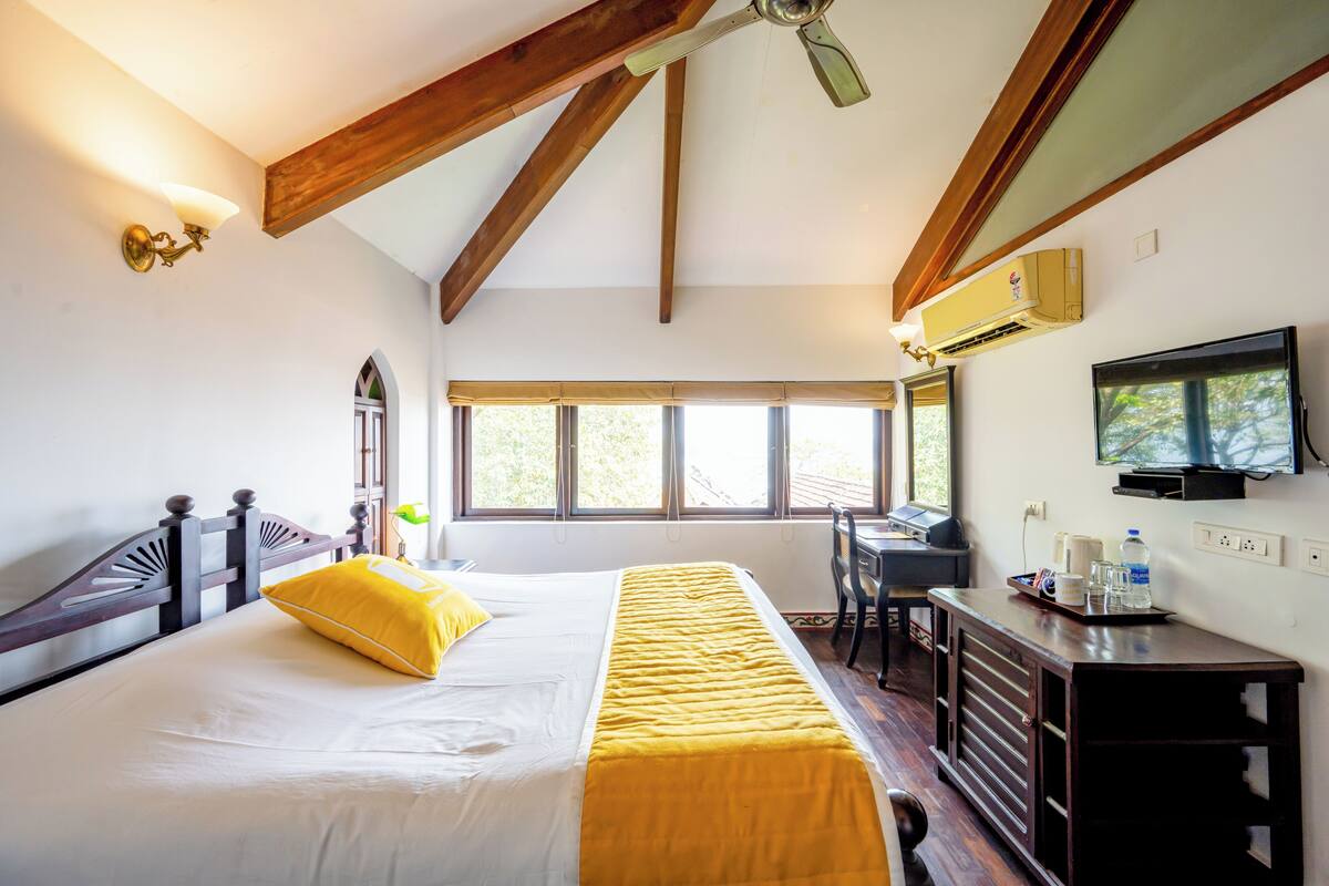 A bedroom with a bed, a desk, a chair, a TV, and a ceiling fan.