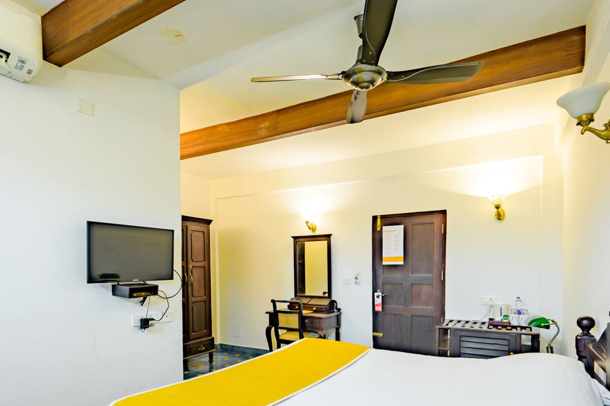 A hotel room with a bed, a desk, a chair, a television, and a ceiling fan.